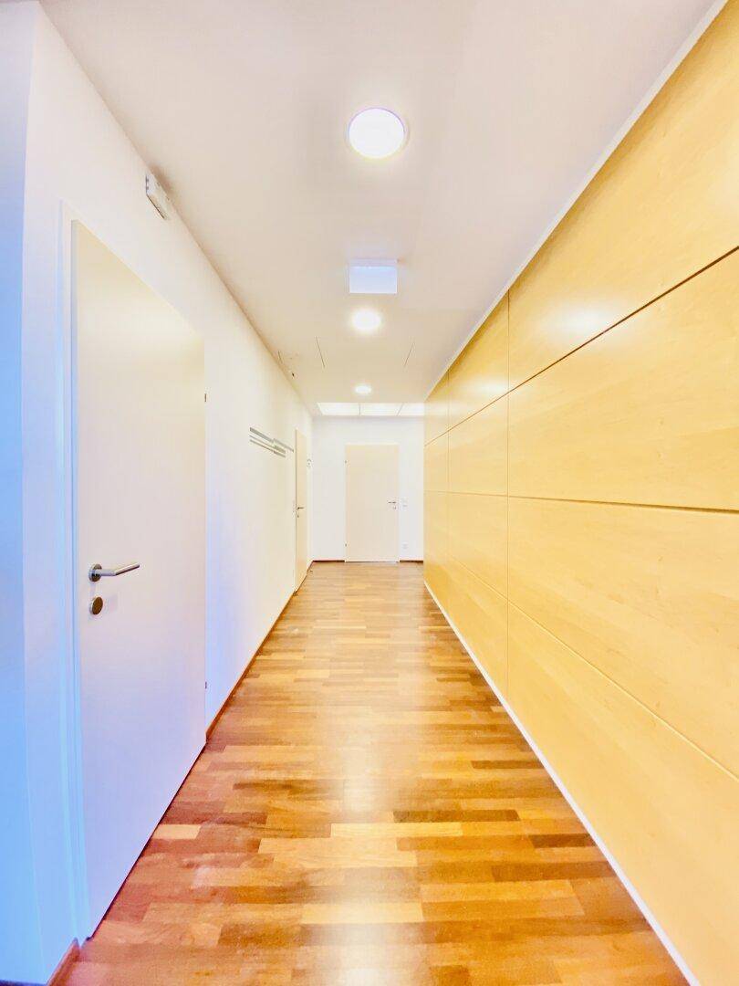 Heller Flur mit Holzboden und eleganter Holzverkleidung an der Wand, führt zu weiteren Räumen.