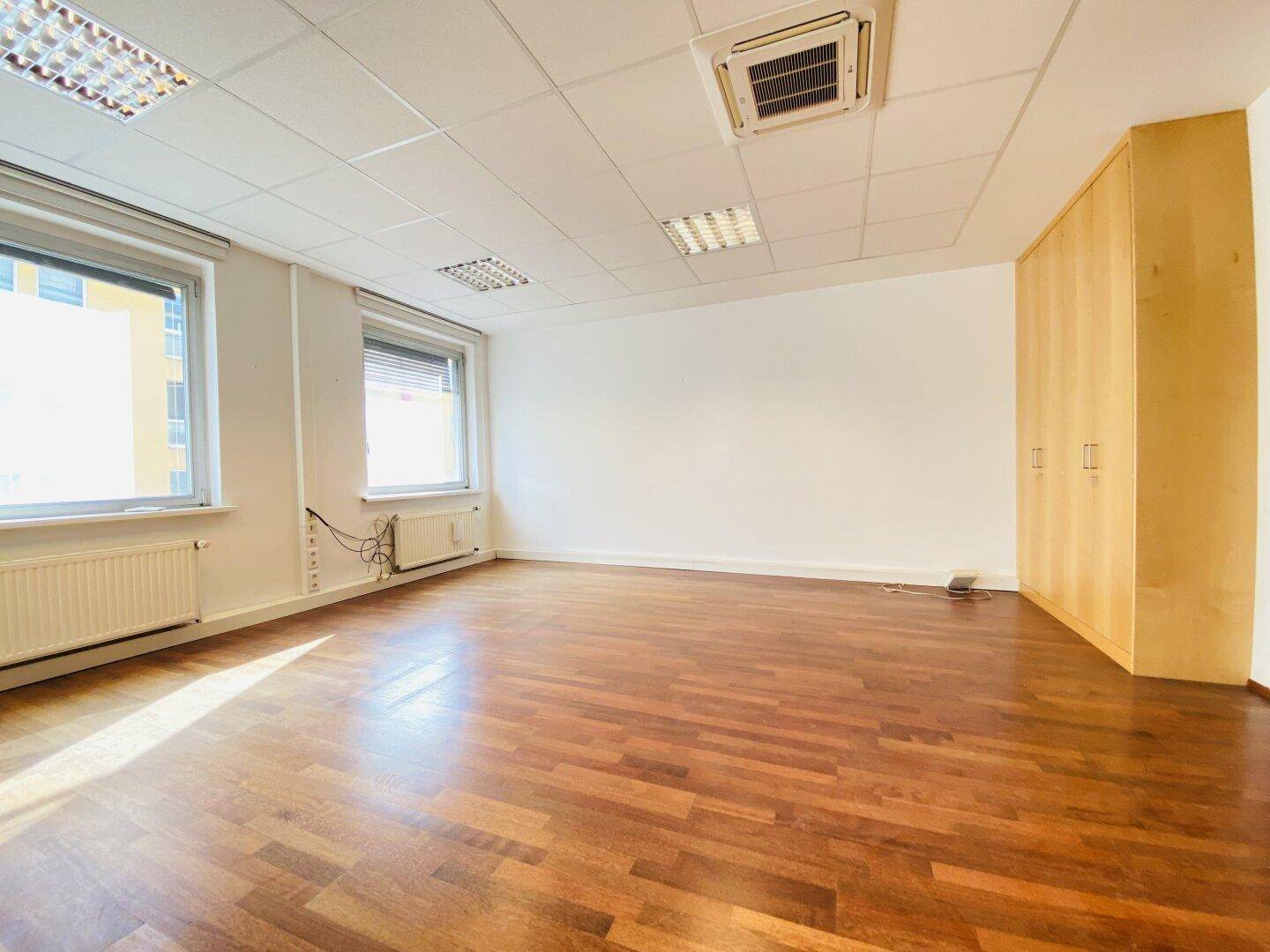 Geräumiges Büro mit Holzboden, großen Fenstern und eingebautem Holzschrank, bietet viel Stauraum.