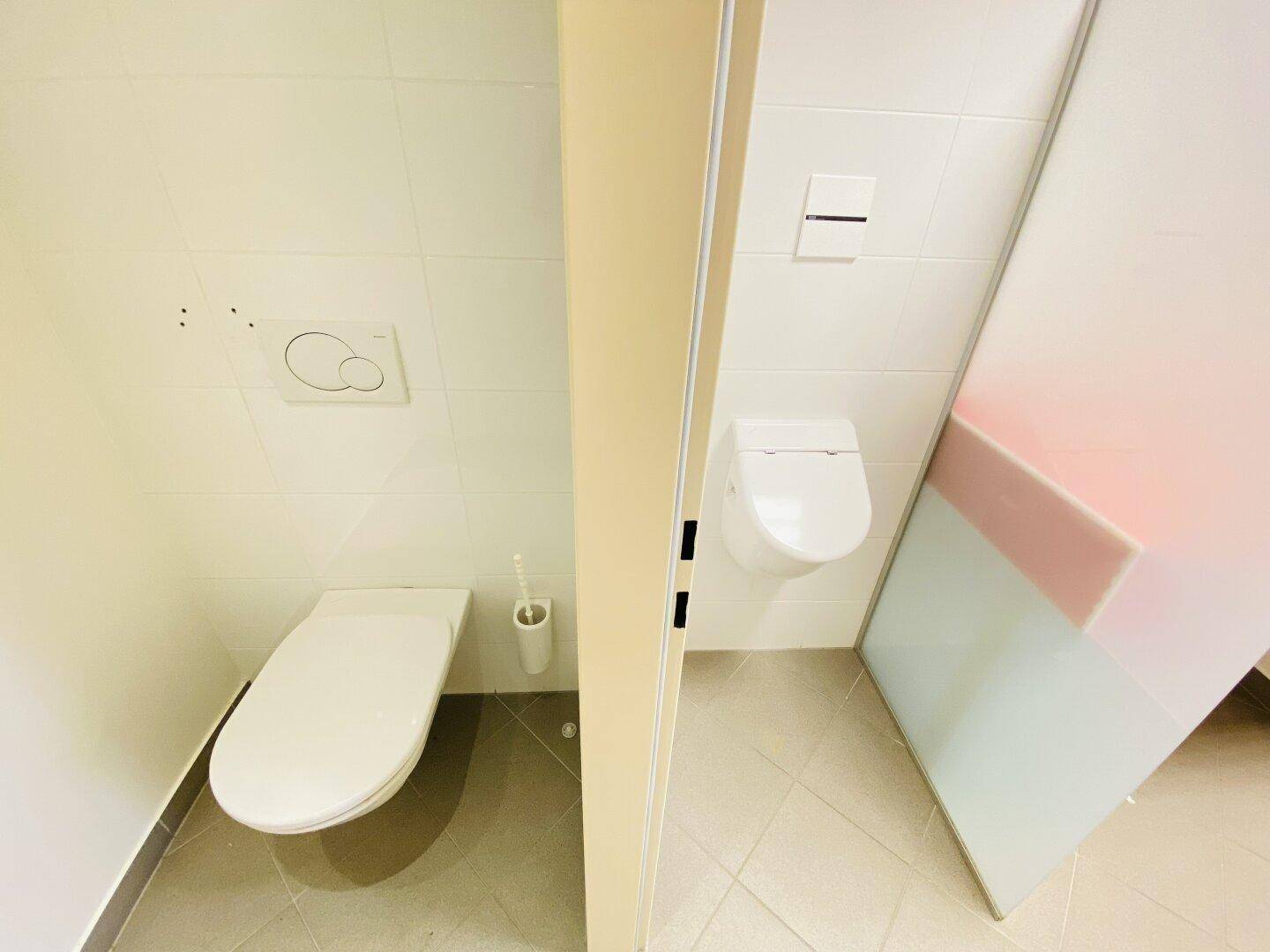 Zwei separate Toilettenkabinen mit modernen Wand-WCs und Fliesenboden, sauber und funktional gestaltet.