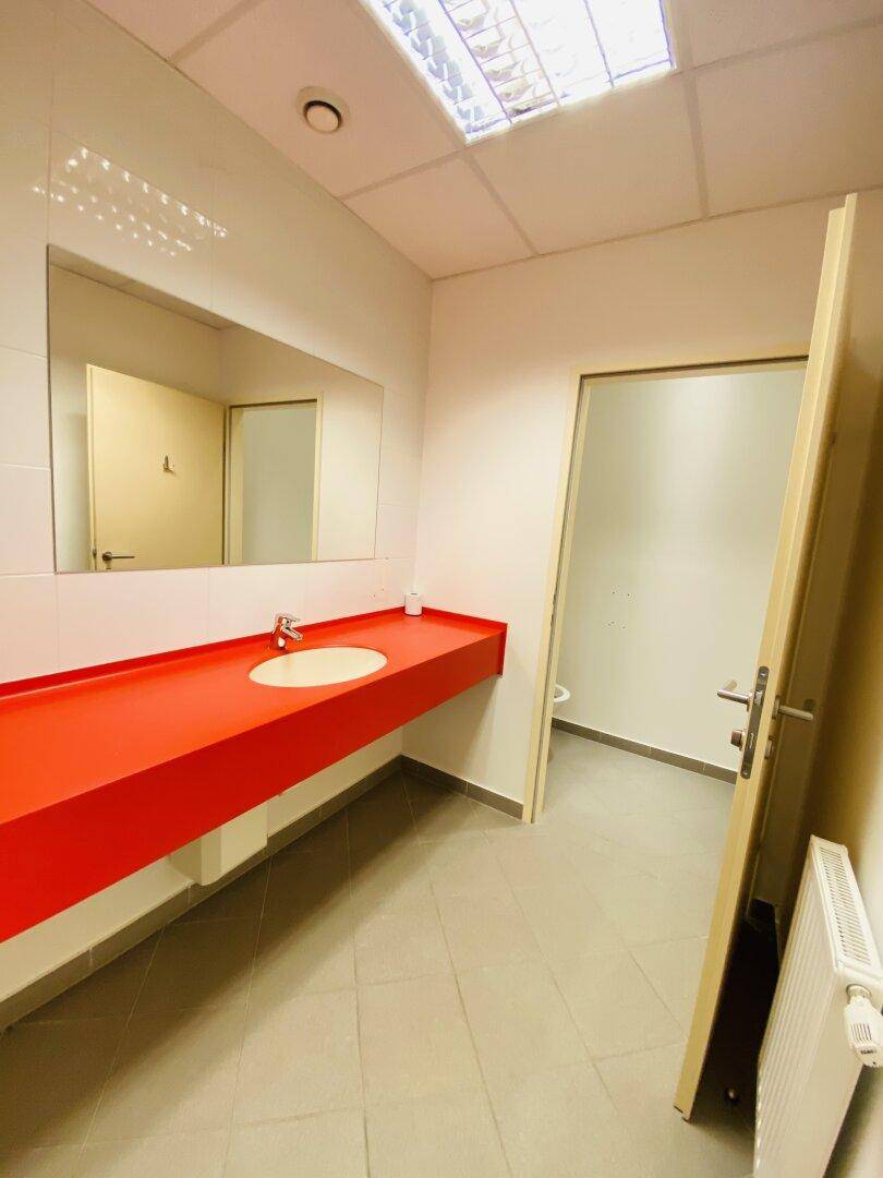 Modernes Badezimmer mit rotem Waschtisch, großem Spiegel und Fliesenboden, hell und ansprechend gestaltet.