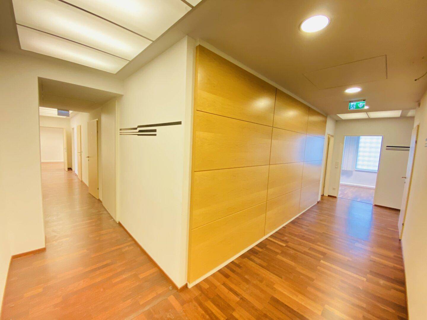 Heller Flur mit Holzboden und Holzverkleidung, der zu weiteren Büroräumen und Arbeitsbereichen führt.