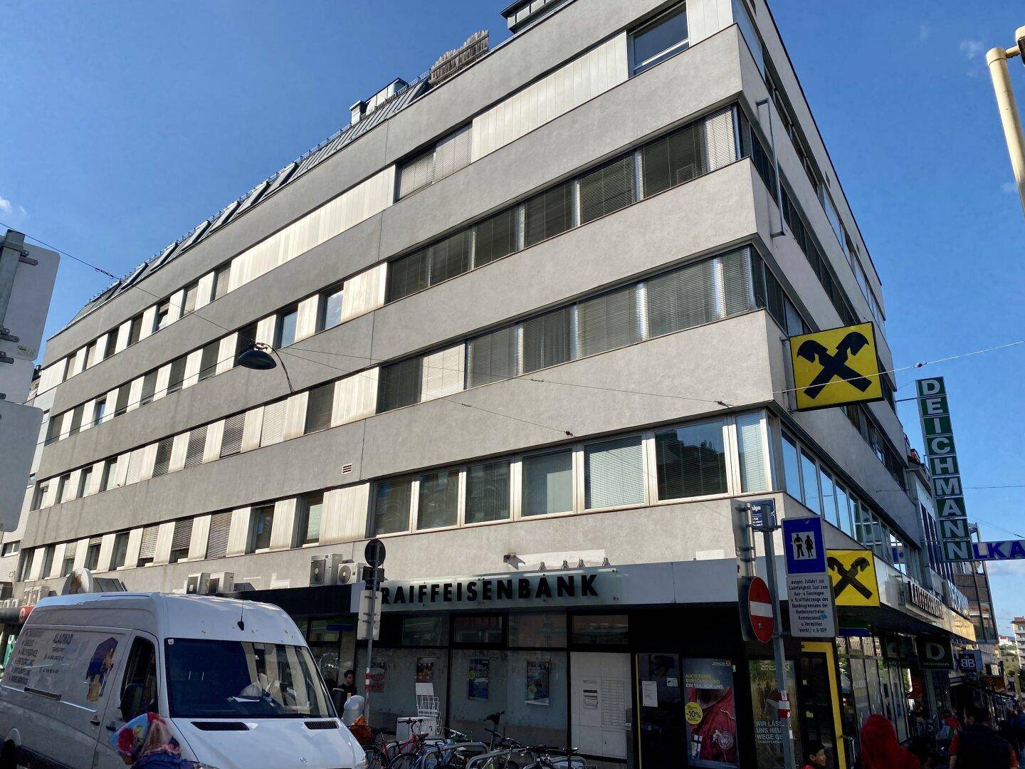 Mehrstöckiges Geschäftsgebäude mit moderner Fassade und Raiffeisenbank im Erdgeschoss, gelegen an einer belebten Straße.