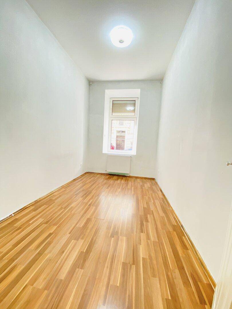 Schmaler Raum mit Laminatboden und einem Fenster, ideal als kleines Schlafzimmer oder Arbeitszimmer.