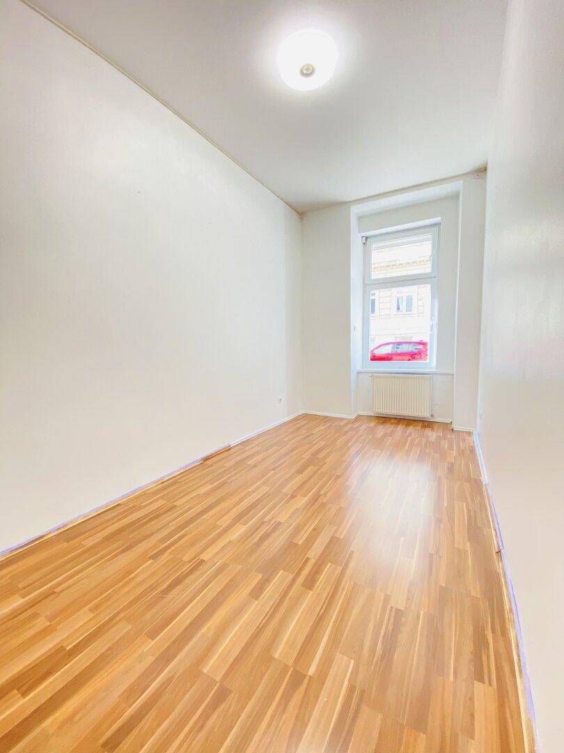 Helles Schlafzimmer mit Laminatboden und einem Fenster mit Blick auf die Straße.