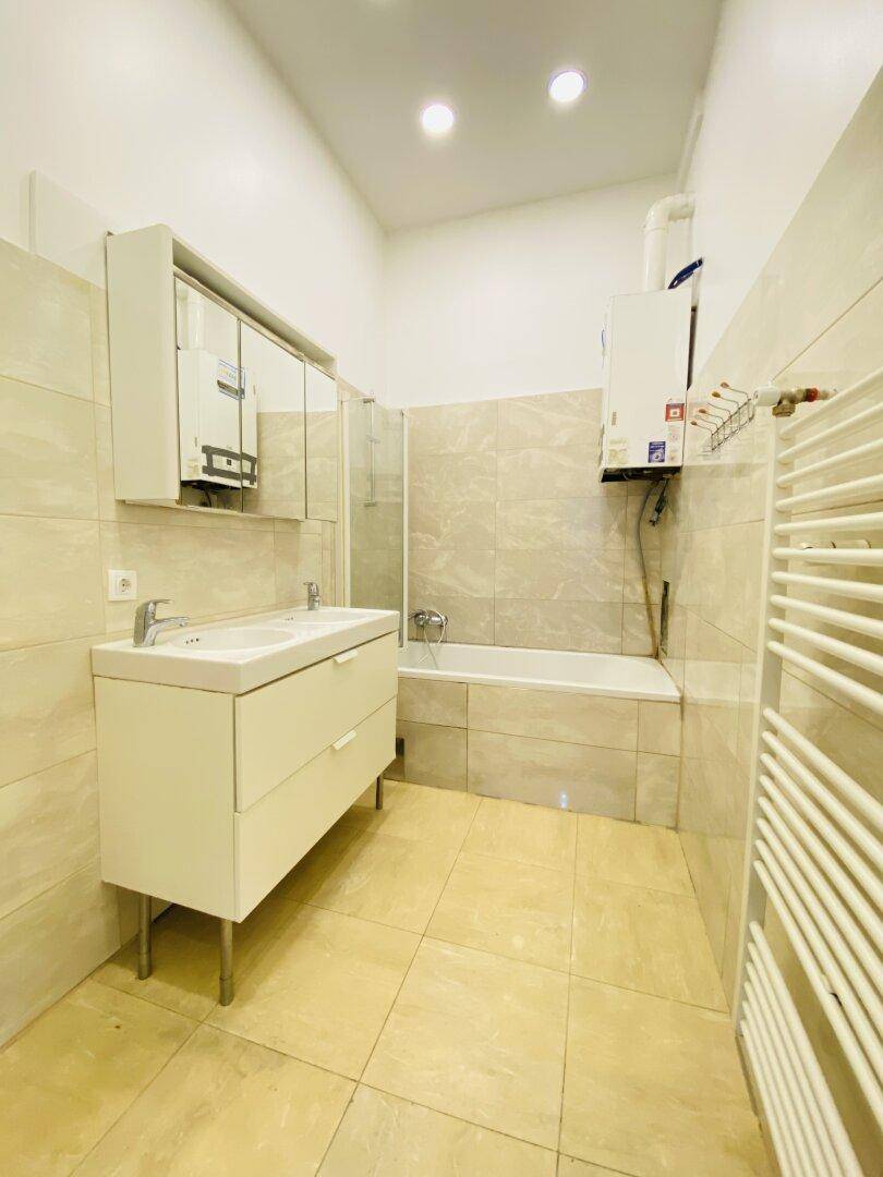 Modernes Badezimmer mit beigen Fliesen, Doppelwaschbecken, Badewanne mit Duschwand und beheiztem Handtuchhalter.