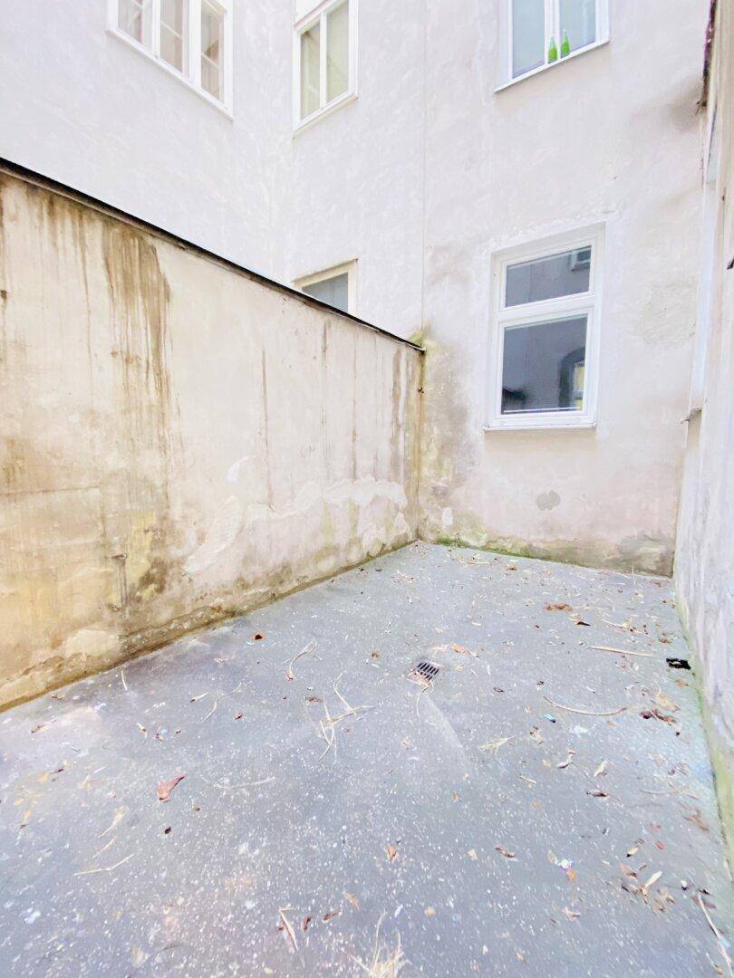 Kleiner, einfacher Außenbereich mit Betonboden und hohen Mauern, der als Patio genutzt werden könnte.