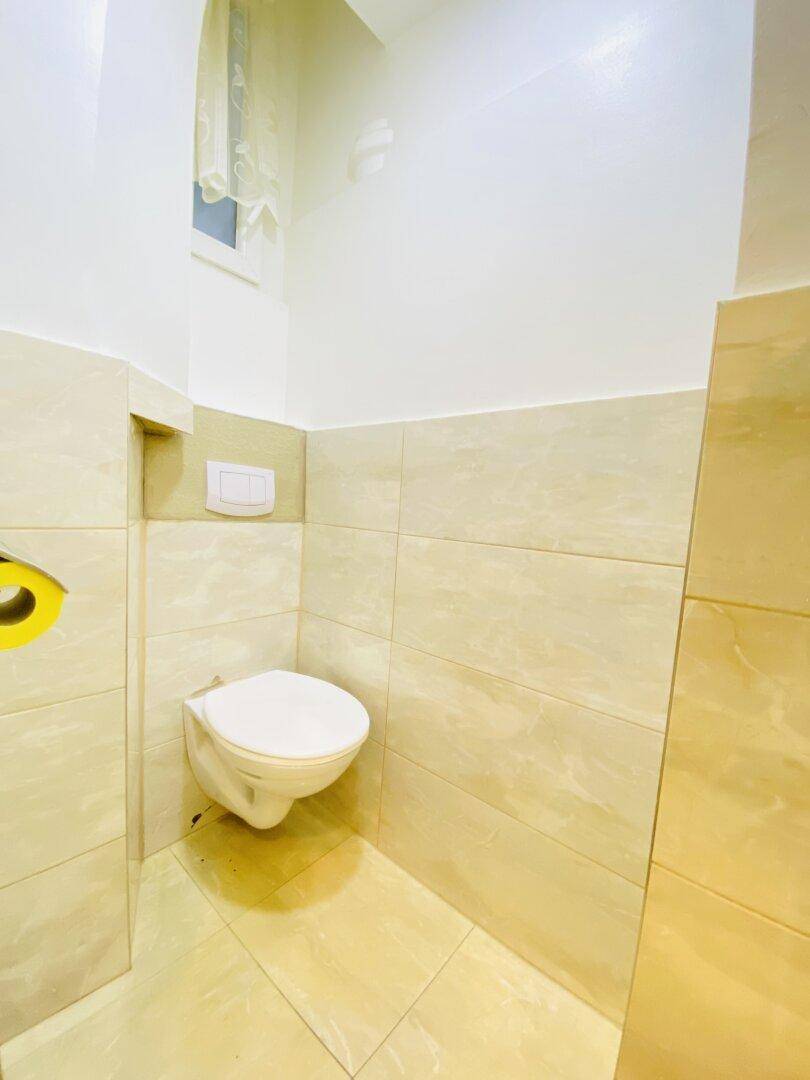 Kleines WC mit wandhängender Toilette, beigen Fliesen und einem kleinen Fenster für Tageslicht.