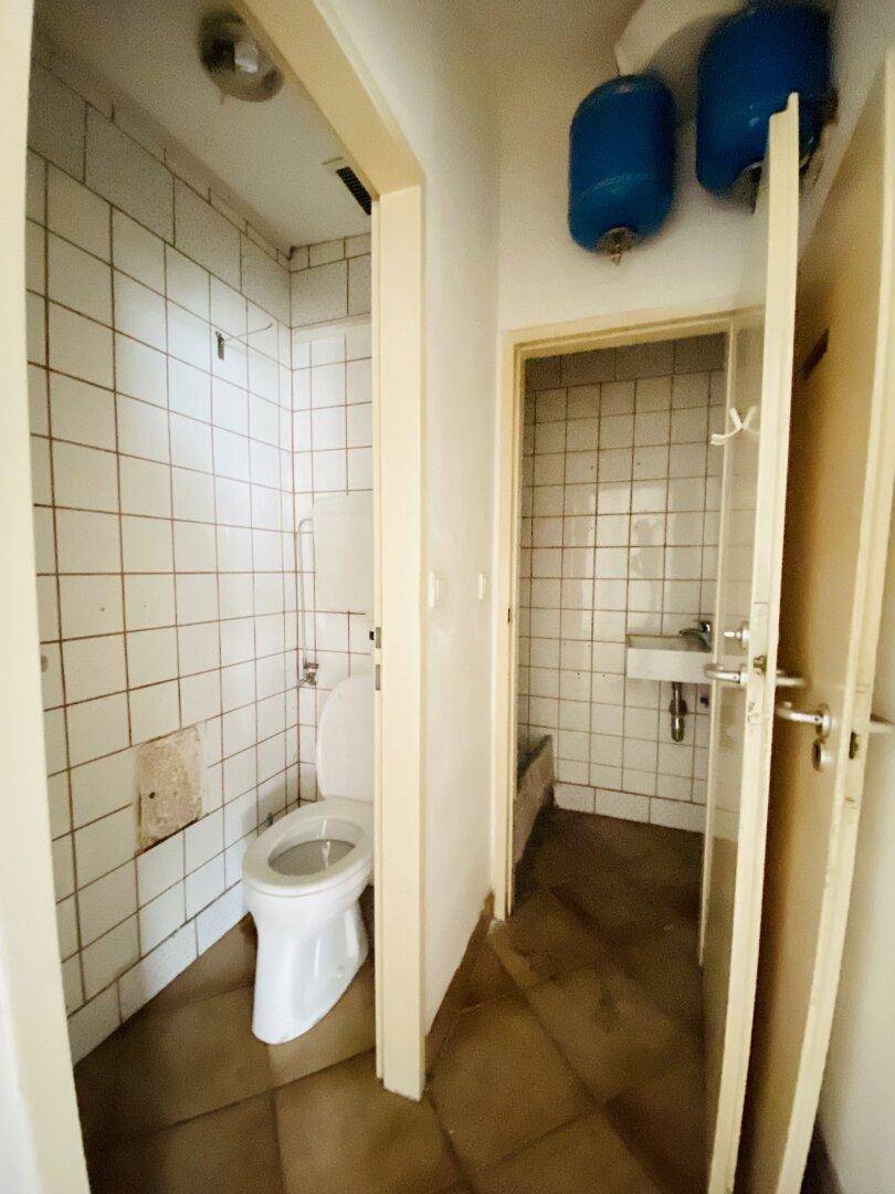 Zwei separate kleine Badezimmer mit weißen Fliesen, Toilette, Waschbecken und Warmwasserbereitern in einfachem Zustand.