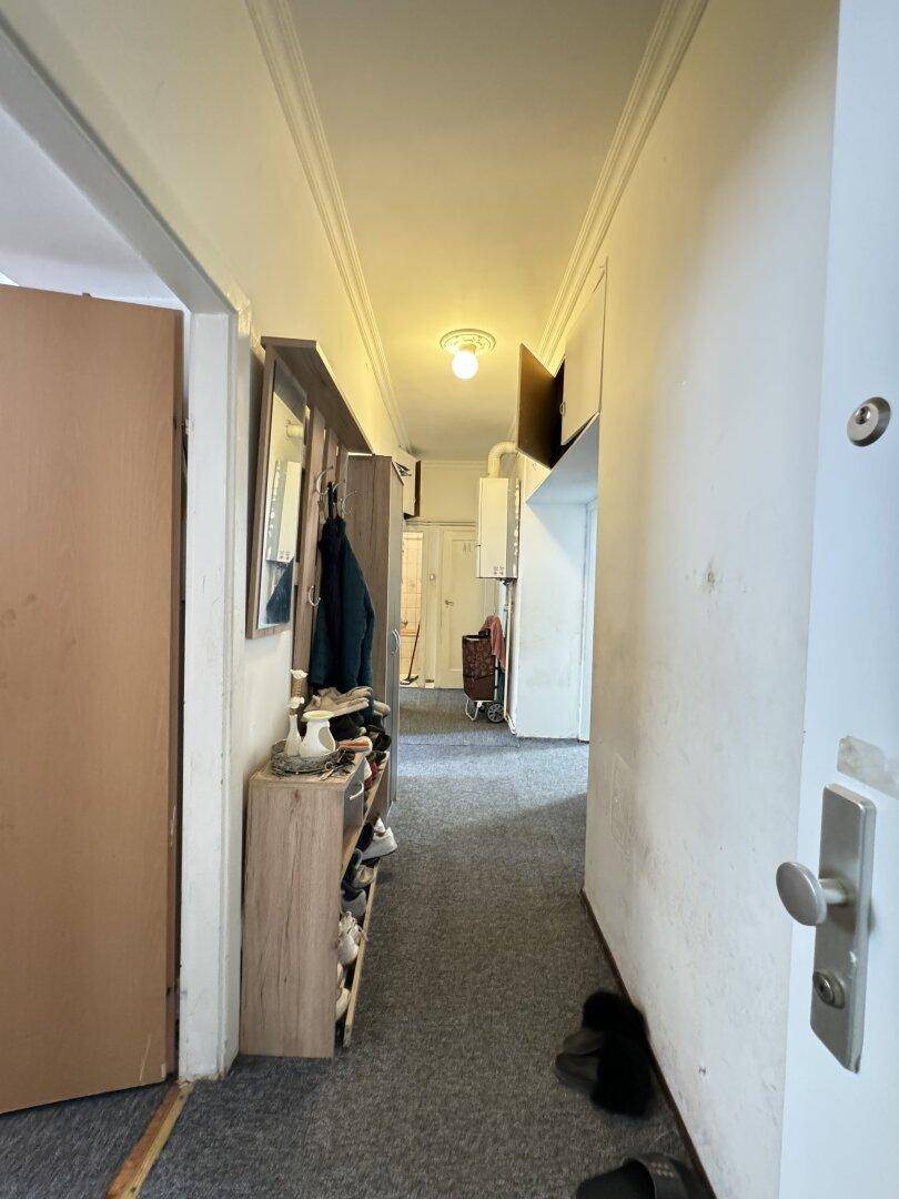 Schmaler Flur mit Schuhregal und Garderobe, der zu weiteren Räumen führt.