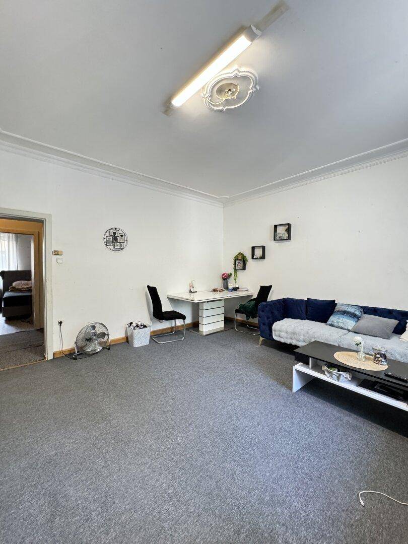 Heller Wohnbereich mit Esstisch und Zugang zu einem weiteren Zimmer, ausgestattet mit grauem Teppich.
