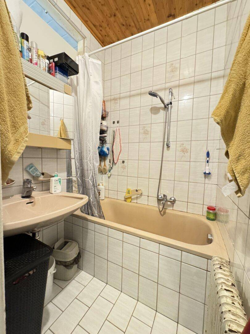 Badezimmer mit beiger Badewanne, Waschbecken und weißen Fliesen, mit Holzdecke.