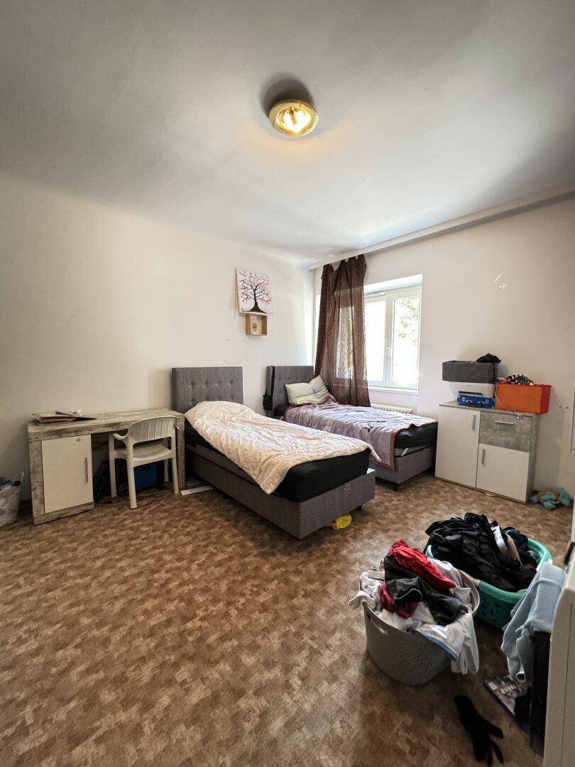 Schlafzimmer mit zwei Einzelbetten, einem Schreibtisch und gemustertem PVC-Bodenbelag.