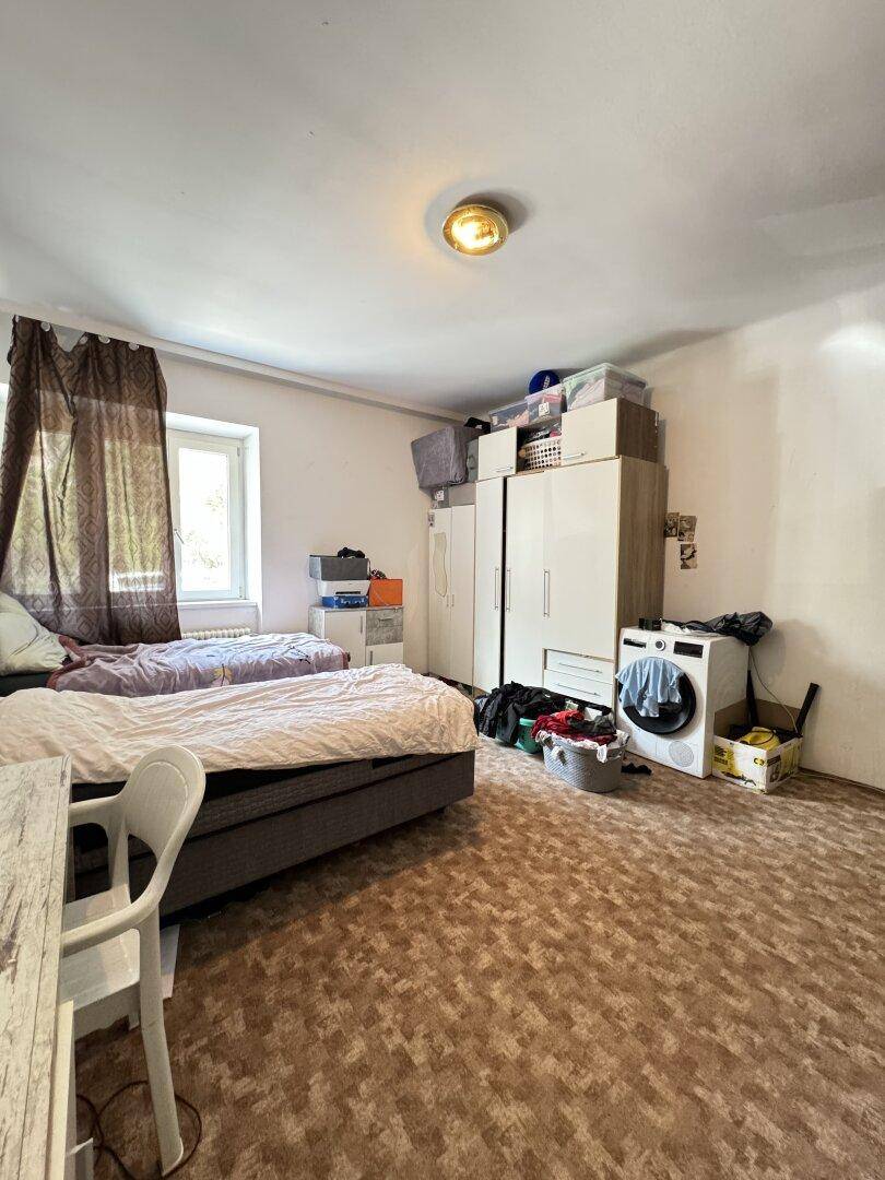 Schlafzimmer mit Kleiderschränken, zwei Betten und einer Waschmaschine, mit Fenster für Tageslicht.