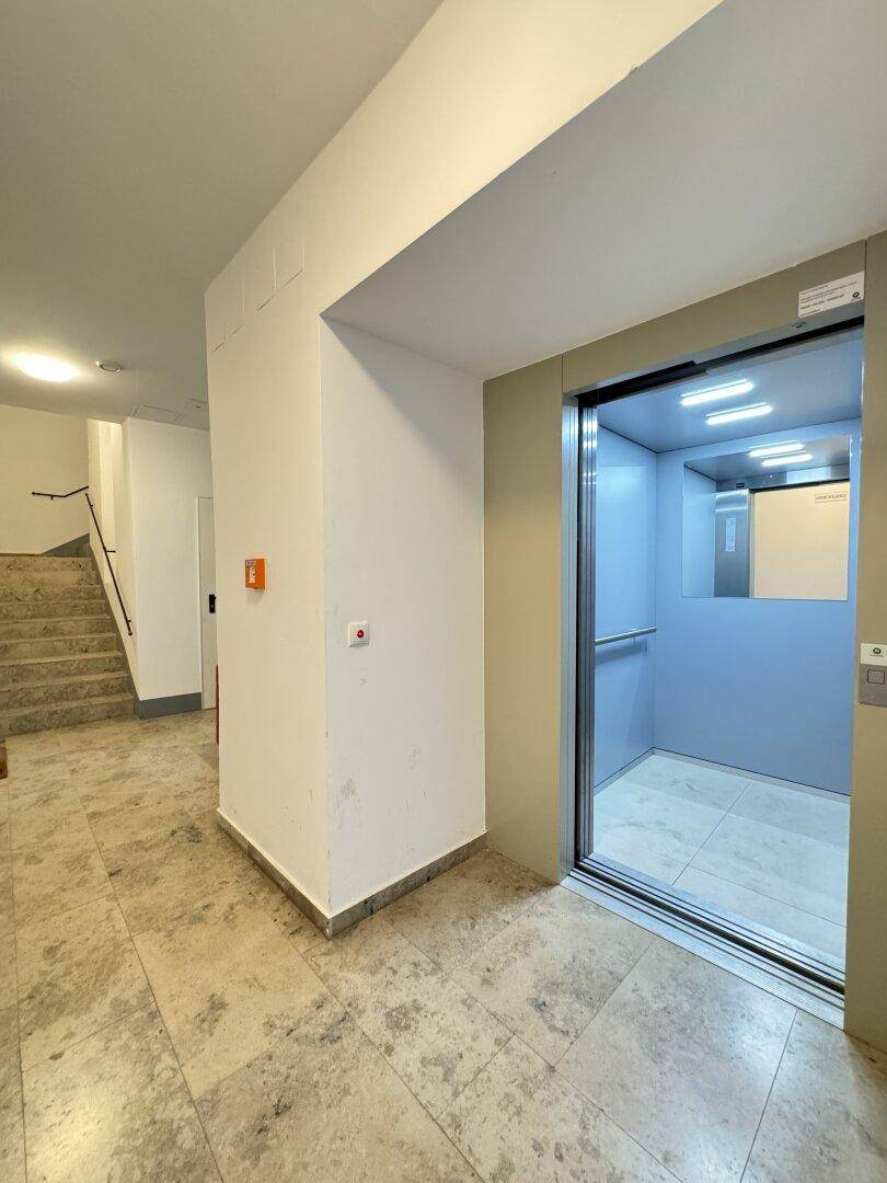 Heller Eingangsbereich mit Aufzug und Treppenhaus, ausgestattet mit Steinboden.