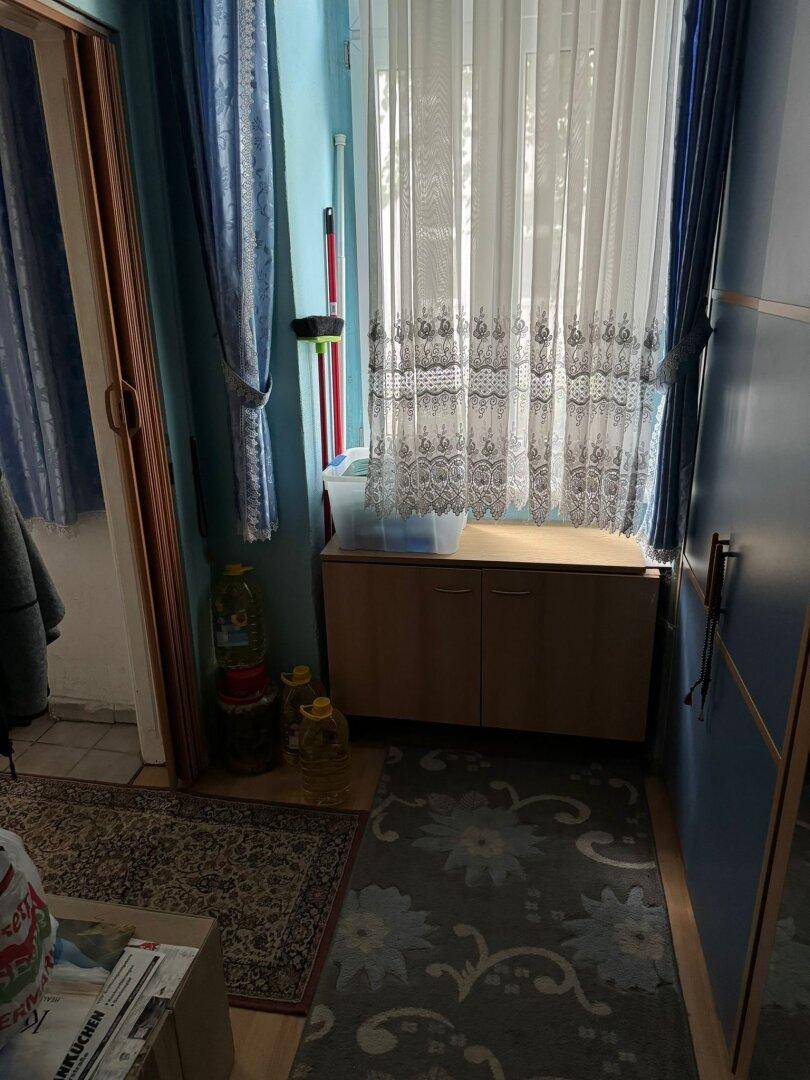 Schmaler Flur mit Fenster, Vorhängen und einem kleinen Holzschrank.