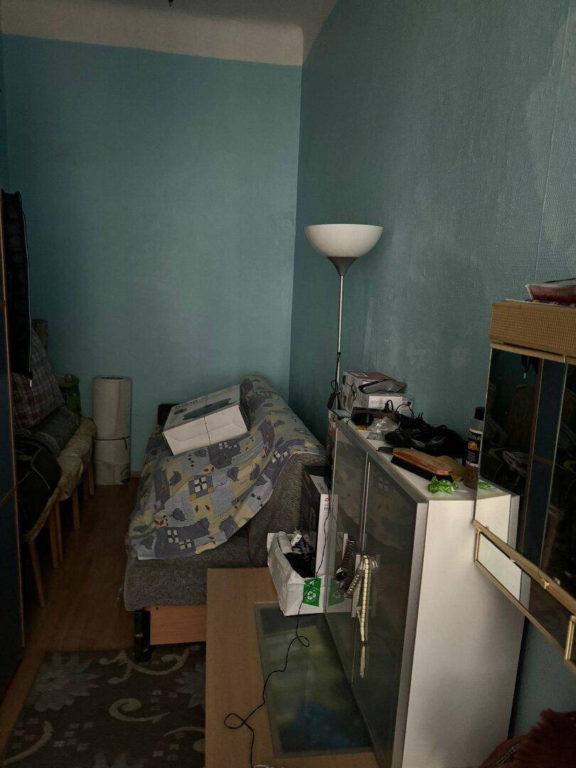 Wohnzimmer mit Sofa, Stehlampe und einem Schrank, in einem eher dunklen Bereich.