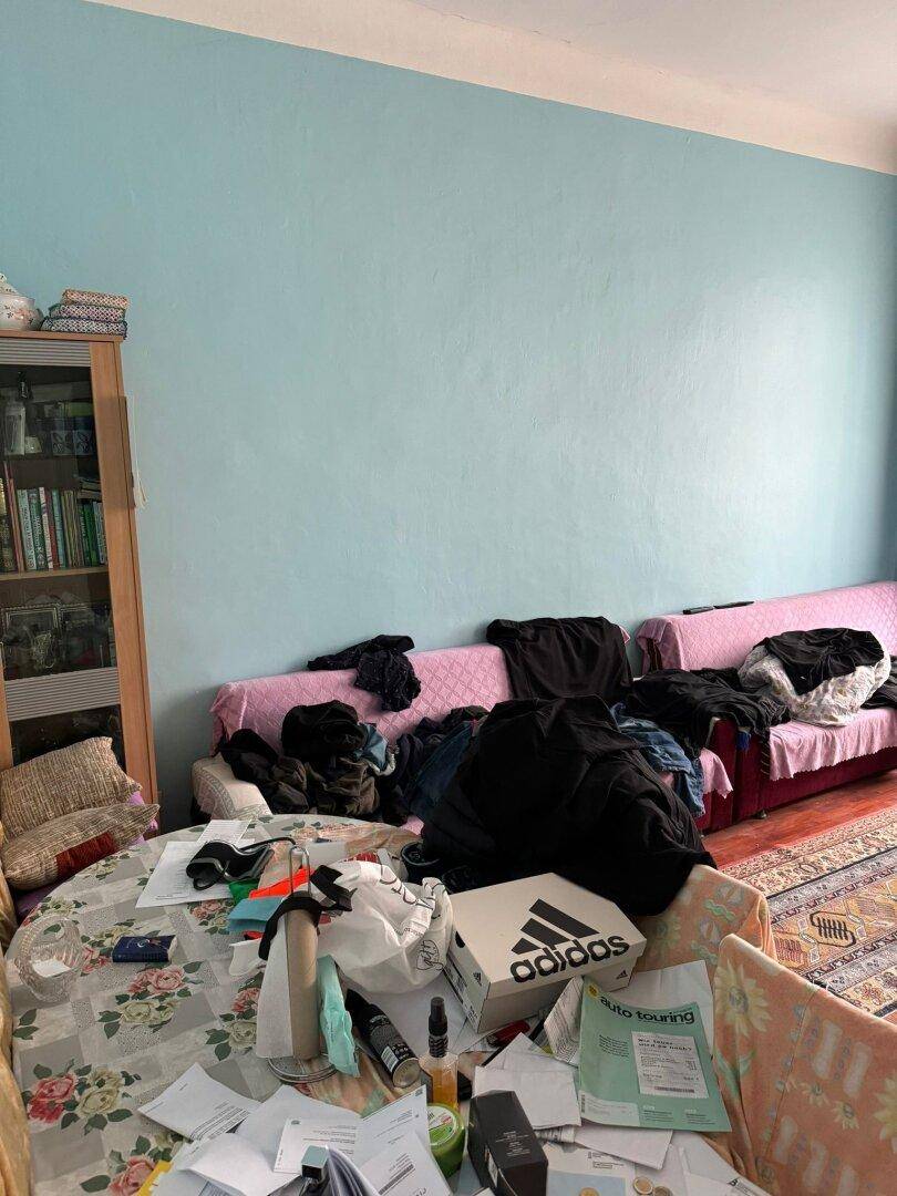 Unaufgeräumtes Wohnzimmer mit hellblauen Wänden, Sofa und einem Tisch voller Gegenstände.
