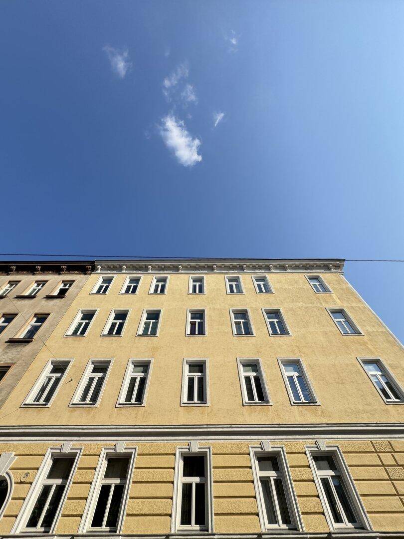 Ansicht einer alten Gebäudefassade mit vielen Fenstern und gelben Wänden unter blauem Himmel.
