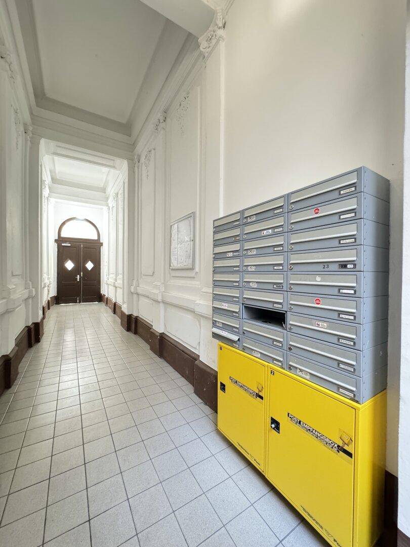 Flur mit Briefkästen an der Seite, Stuckverzierungen und einem Fliesenboden, der zu einer Doppeltür führt.