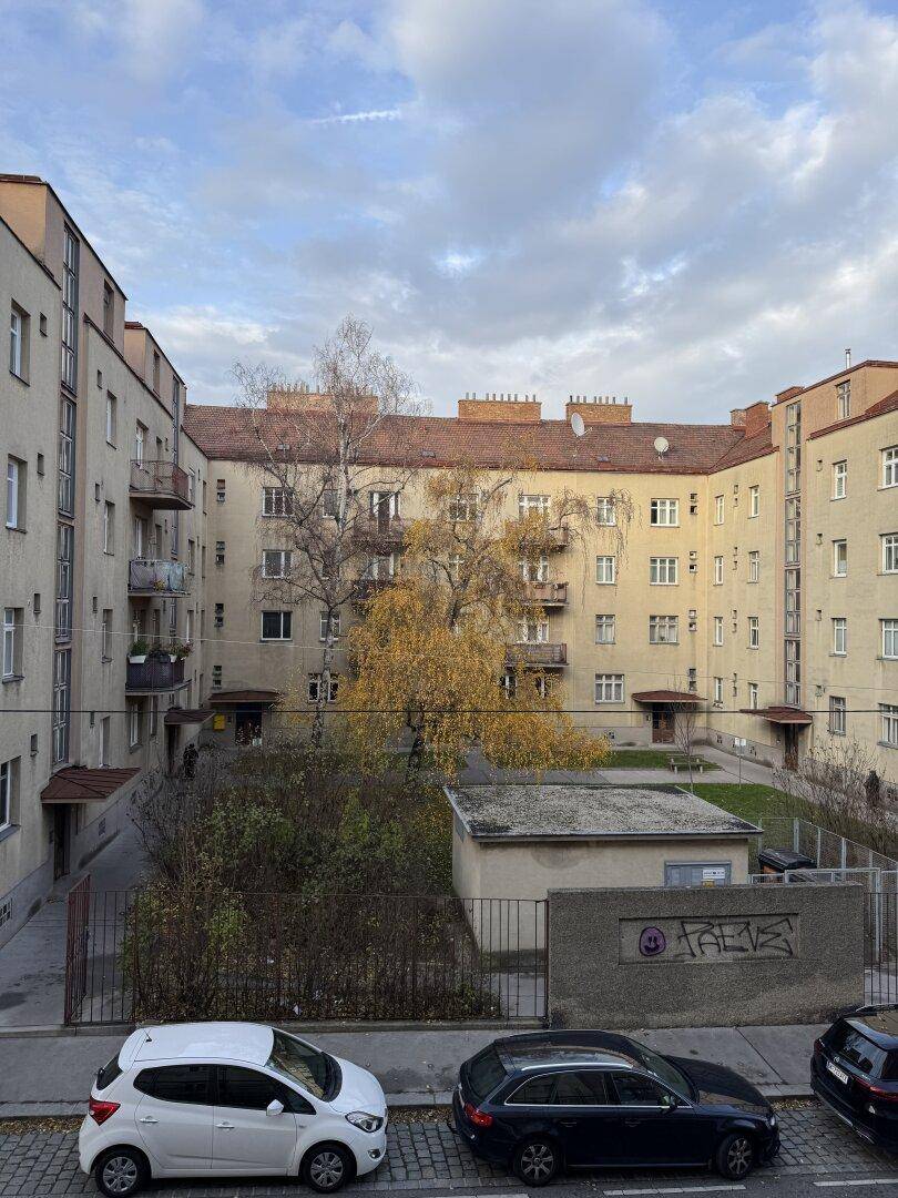 Innenhof einer Wohnanlage mit Bäumen und geparkten Autos, umgeben von Gebäuden.
