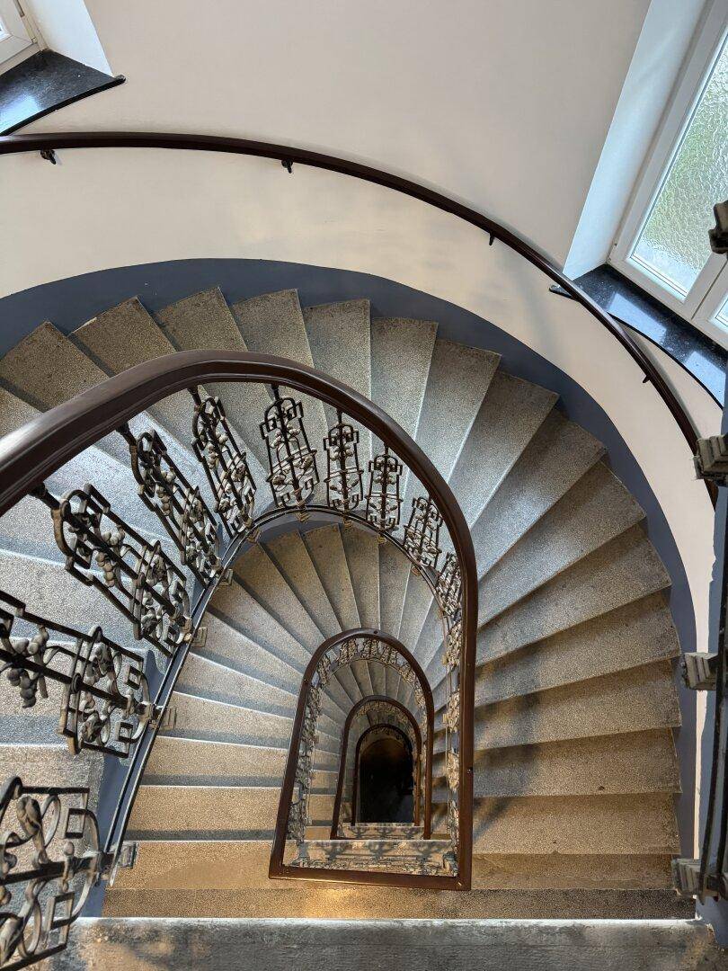 Wendeltreppe in einem Altbau mit steinernen Stufen und kunstvollem Geländer.