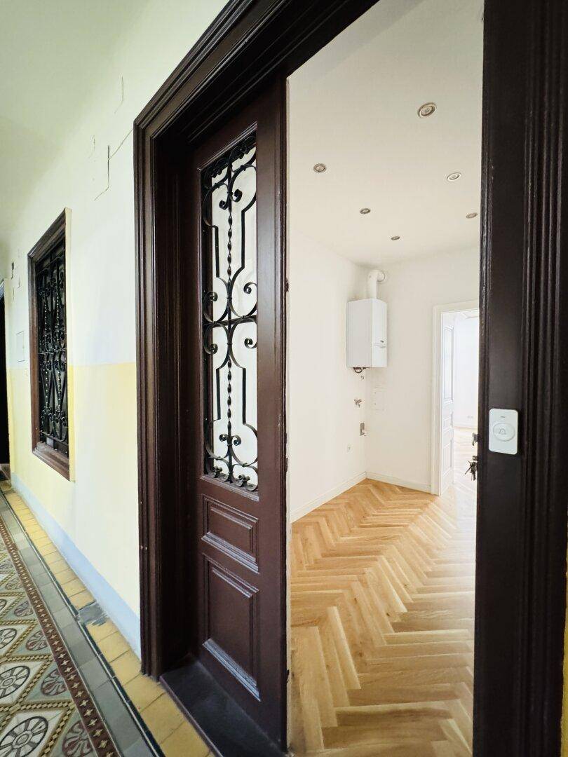 Eingangsbereich der Wohnung mit verzierter Holztür, die in den frisch renovierten Flur führt.