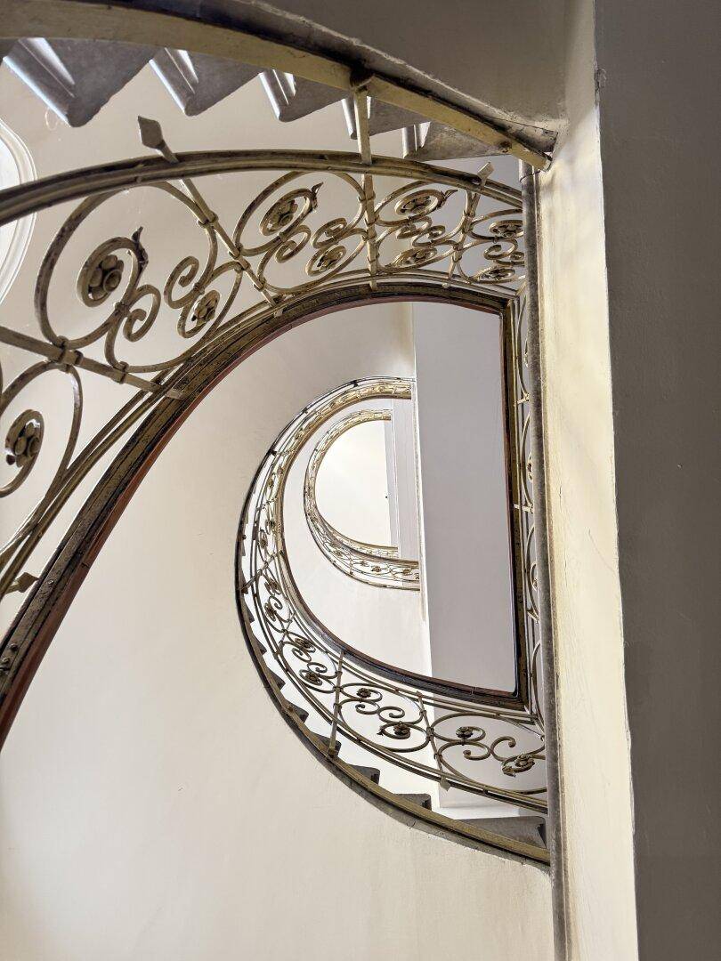 Historisches Treppenhaus mit kunstvollem schmiedeeisernem Geländer und eleganten Stufen.