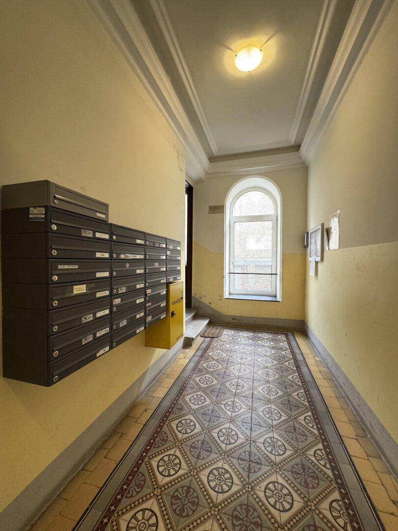 Eingangsbereich eines Altbaus mit historischen Fliesen, Briefkästen und einem großen Bogenfenster.