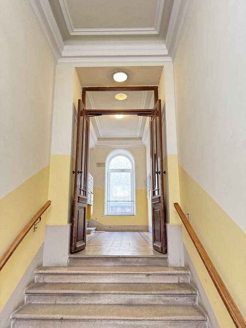 Repräsentativer Eingangsbereich eines Altbaus mit breiter Steintreppe und hohen Holztüren.