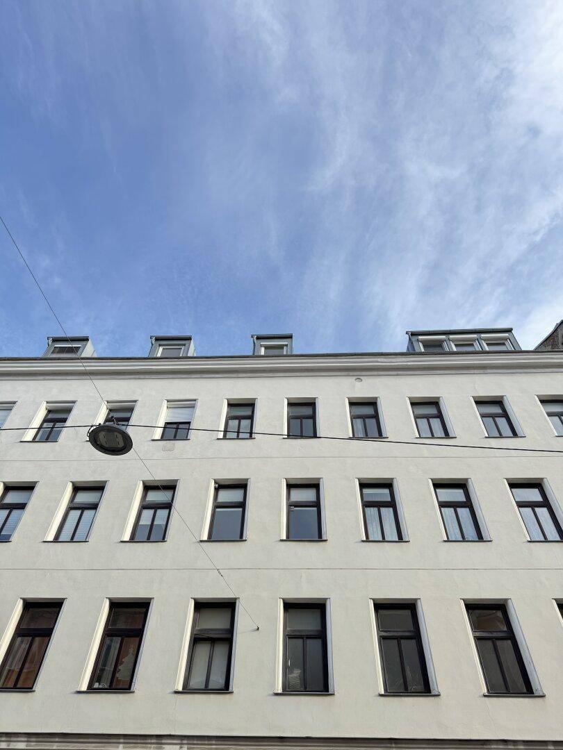 Ansicht der oberen Stockwerke eines Altbaus mit vielen Fenstern unter einem blauen Himmel.