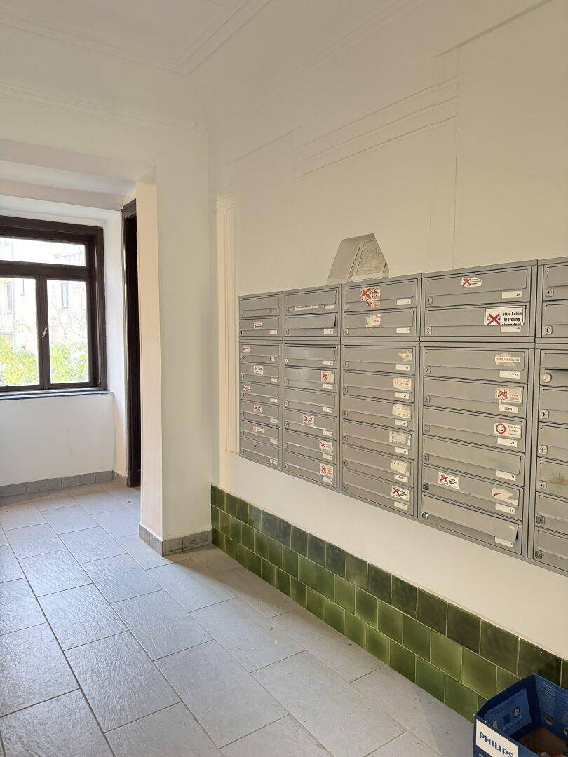 Ein Eingangsbereich mit vielen Briefkästen an der Wand, grünen Fliesen und einem Fenster.
