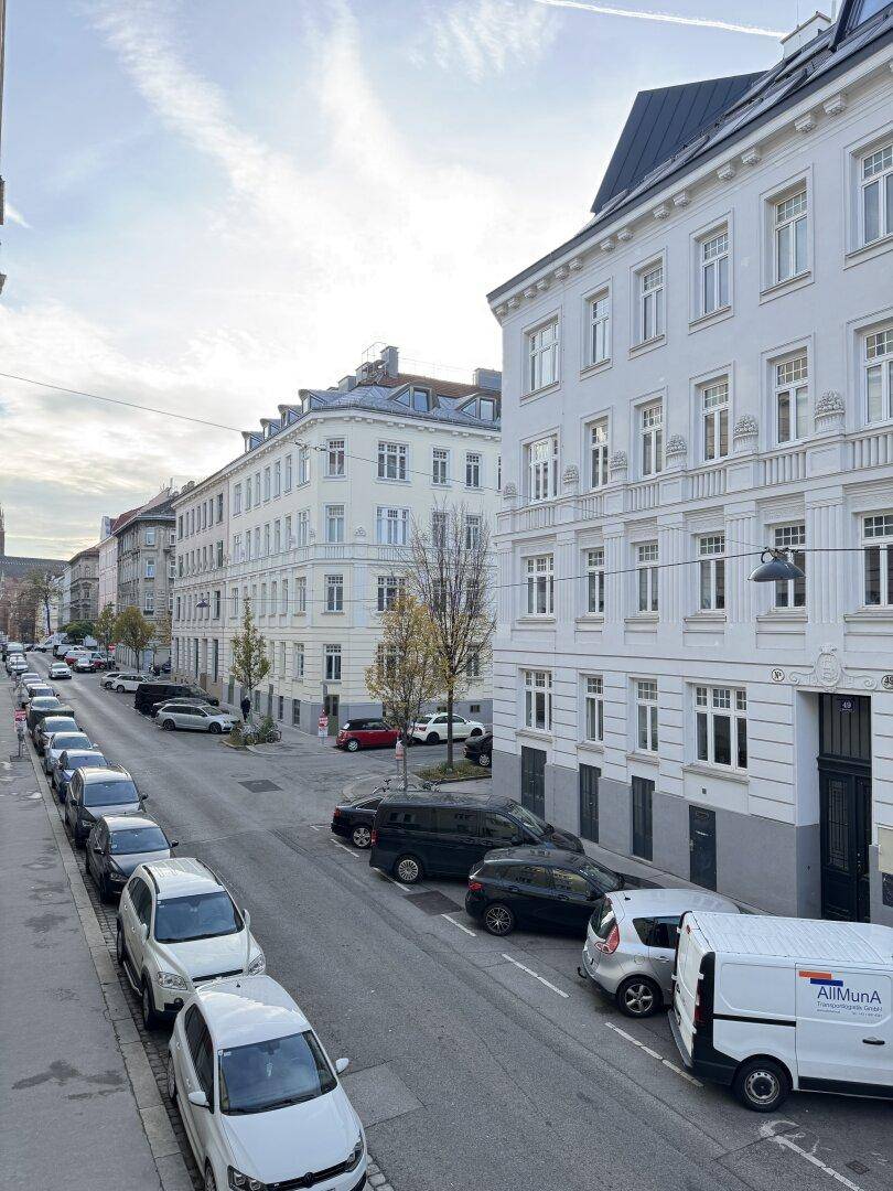 Eine städtische Straße mit vielen parkenden Autos und hohen, hellen Gebäuden auf beiden Seiten.