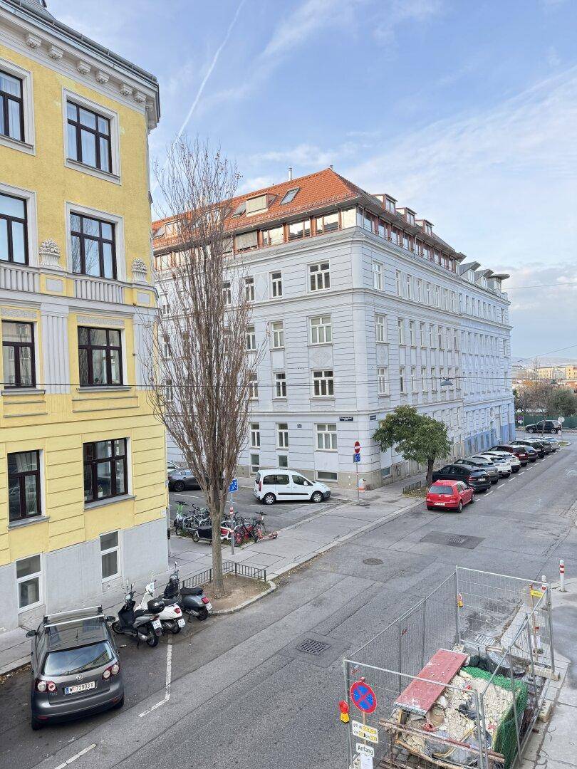 Blick von oben auf eine belebte Stadtstraße mit parkenden Fahrzeugen und umliegenden Gebäuden.