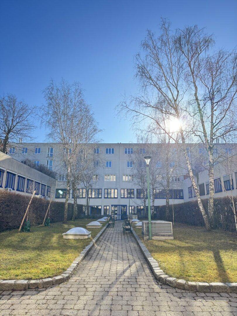 Gebäudekomplex mit Innenhof, gepflegter Grünfläche und Bäumen bei strahlendem Sonnenschein.
