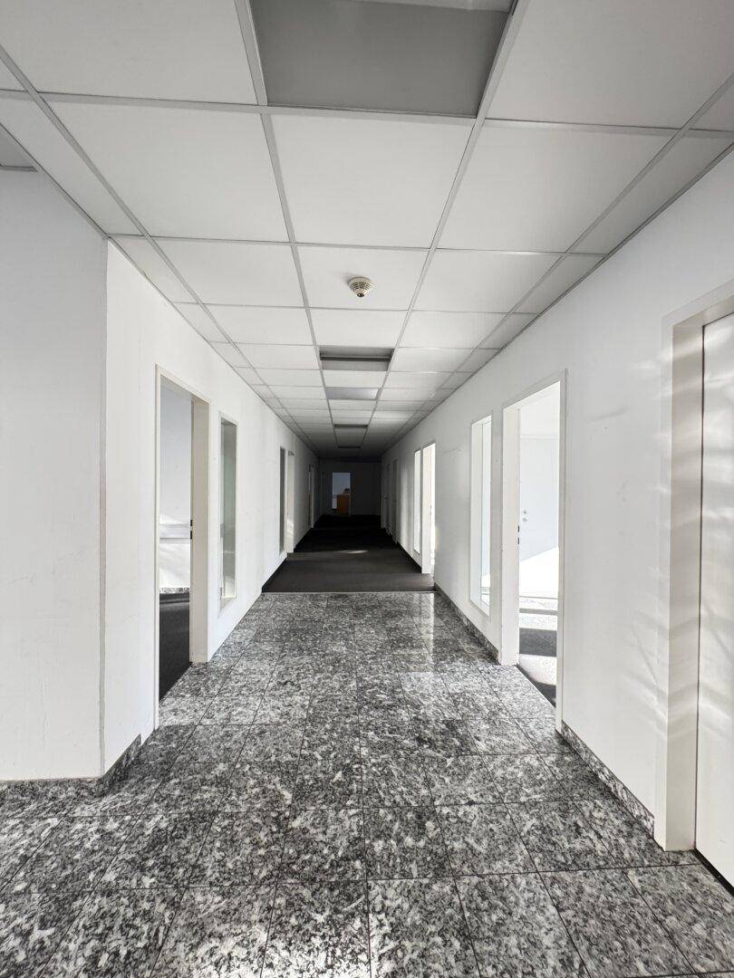 Langer Flur mit grauem Granitfliesenboden und abgehängter Decke, der zu weiteren Räumen führt.