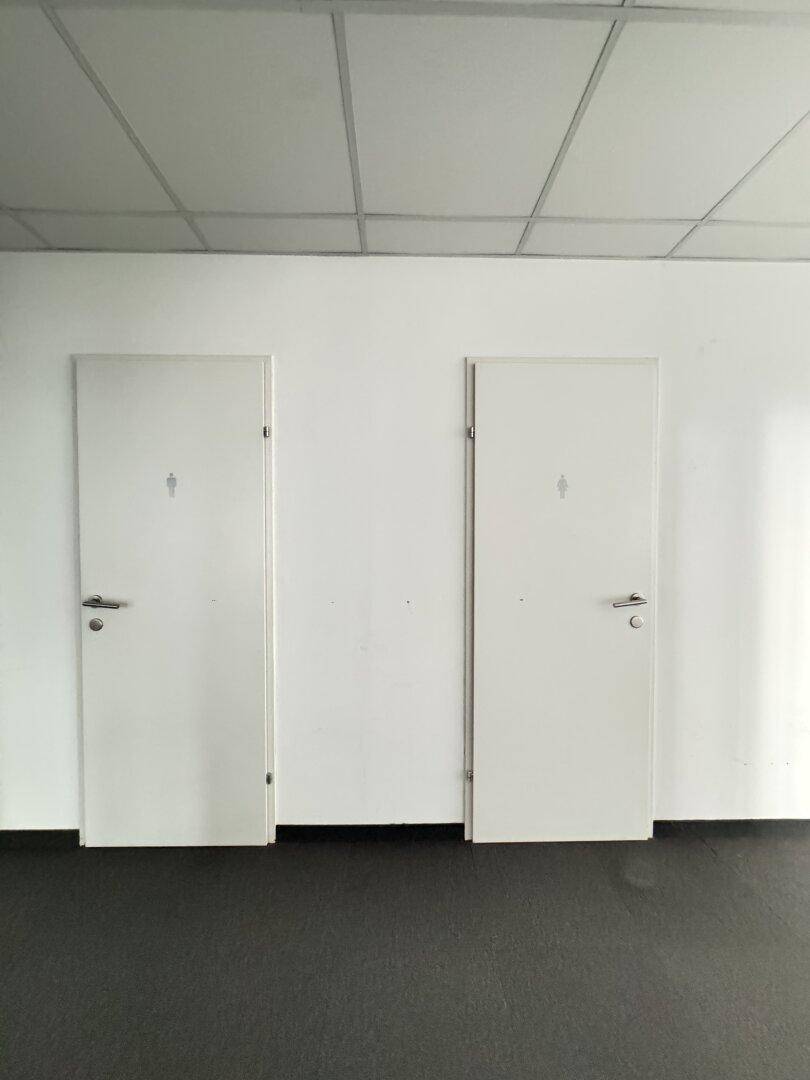 Flur mit zwei Türen zu den Toiletten, dunklem Boden und abgehängter Decke.