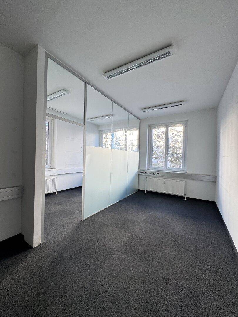 Bürofläche mit Teppichfliesen und einer modernen Glasabtrennung, die den Raum unterteilt.