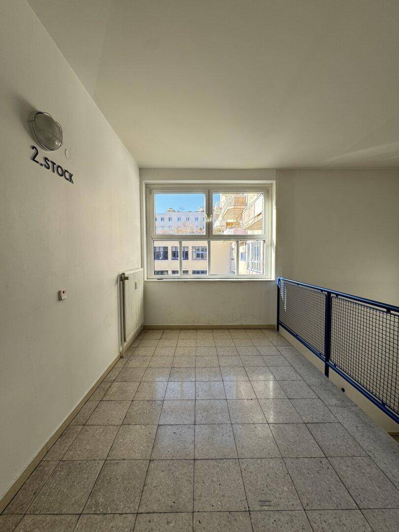 Heller Flurbereich mit Fliesenboden, Fenster und Geländer, das zu einer Treppe führt.