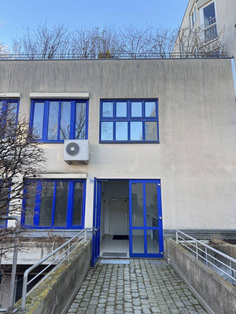 Gebäudeeingang mit blauen Türen und Fenstern, einer Klimaanlage und einer Rampe.