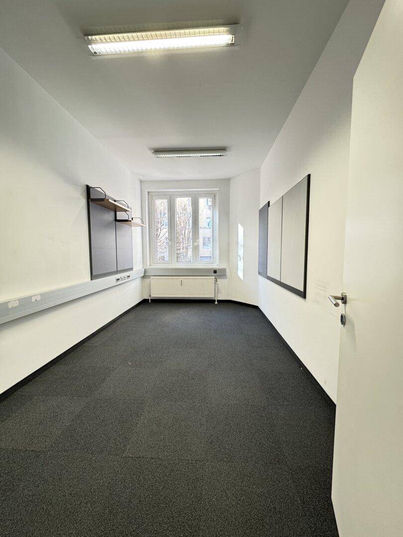Leeres Büro mit Teppichfliesen, einem Fenster und Wandregalen an den Seiten.