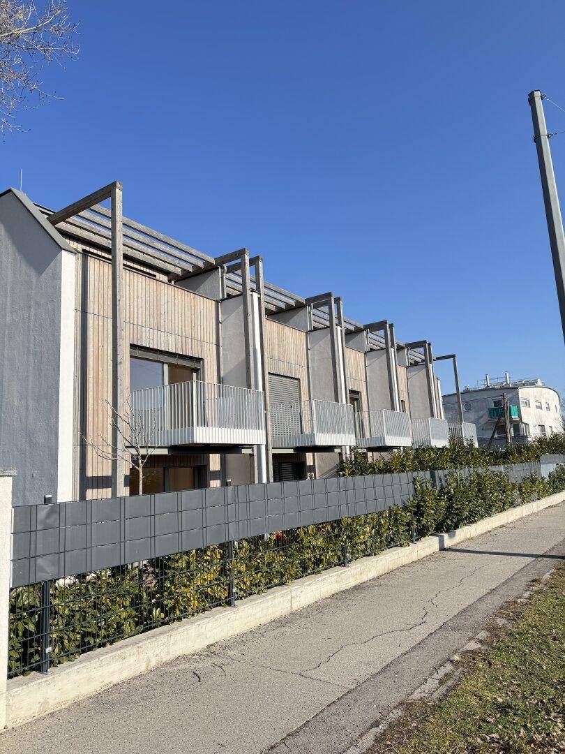 Ansicht moderner Reihenhäuser mit Holzfassaden, Balkonen und gepflegter Hecke.
