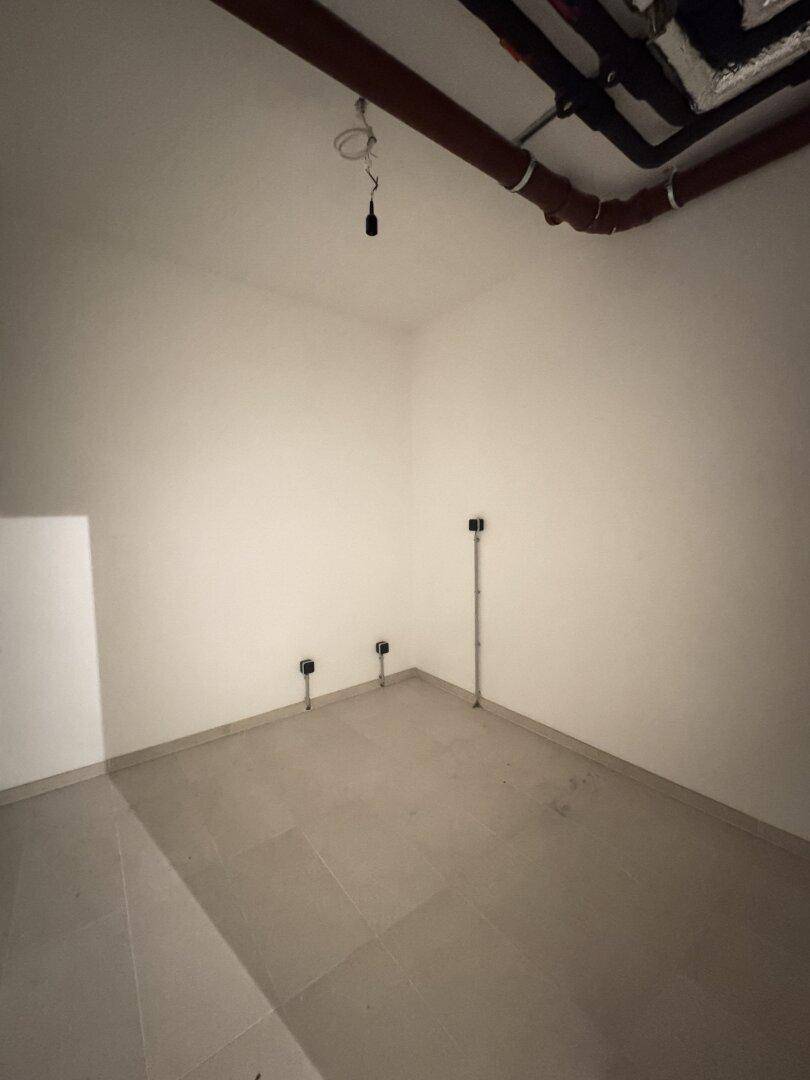 Hauswirtschaftsraum mit sichtbaren Leitungen an der Decke und Anschlüssen an der Wand, gefliester Boden.