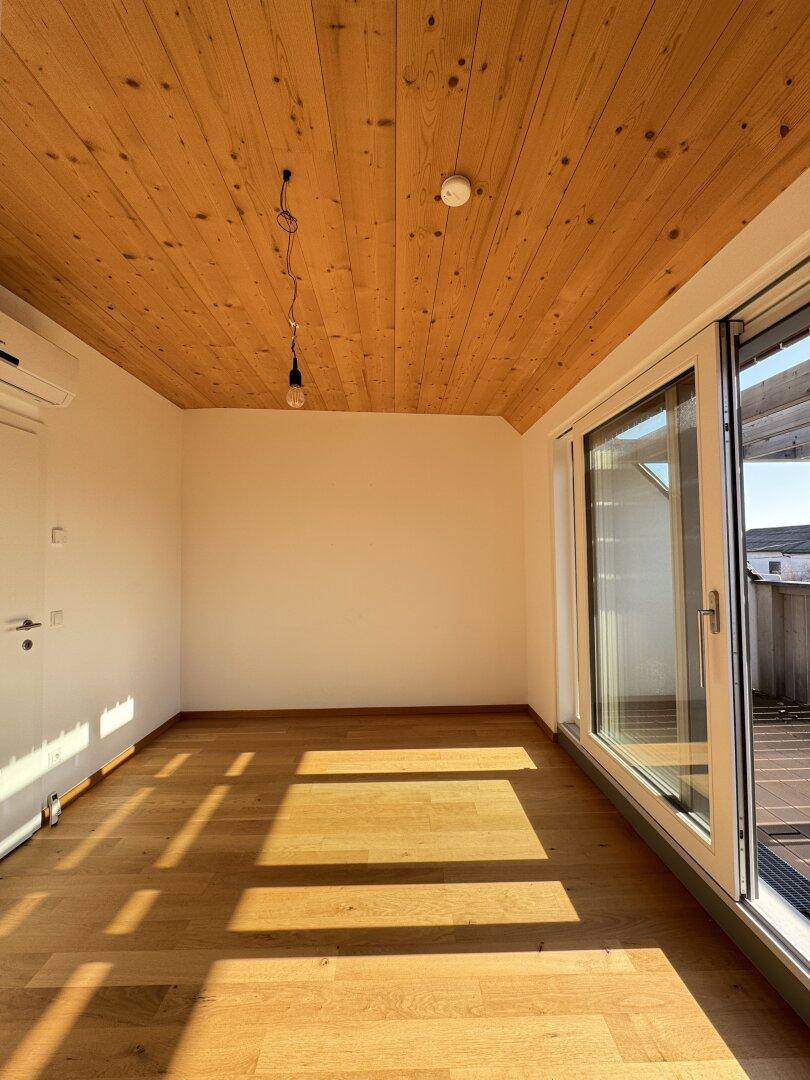 Lichtdurchfluteter Raum mit Holzbalkendecke und hellem Parkettboden, ideal für Wohnzwecke.