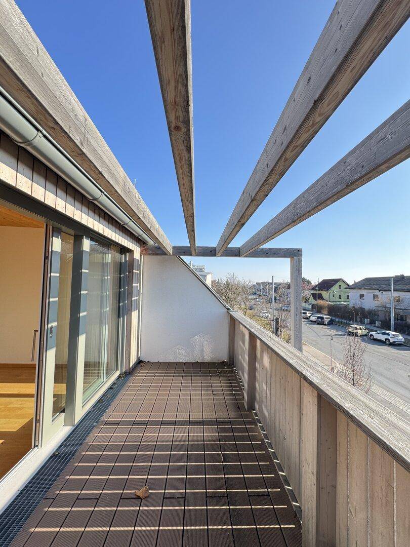 Geräumiger Balkon mit Holzbelag und Pergola, bietet einen Blick auf die Umgebung.