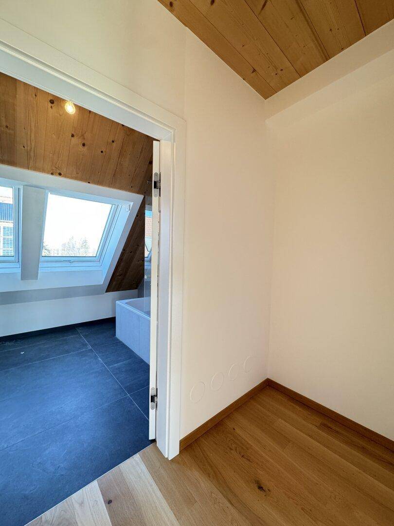 Türöffnung führt in ein modernes Badezimmer mit dunklem Fliesenboden und Dachschräge.