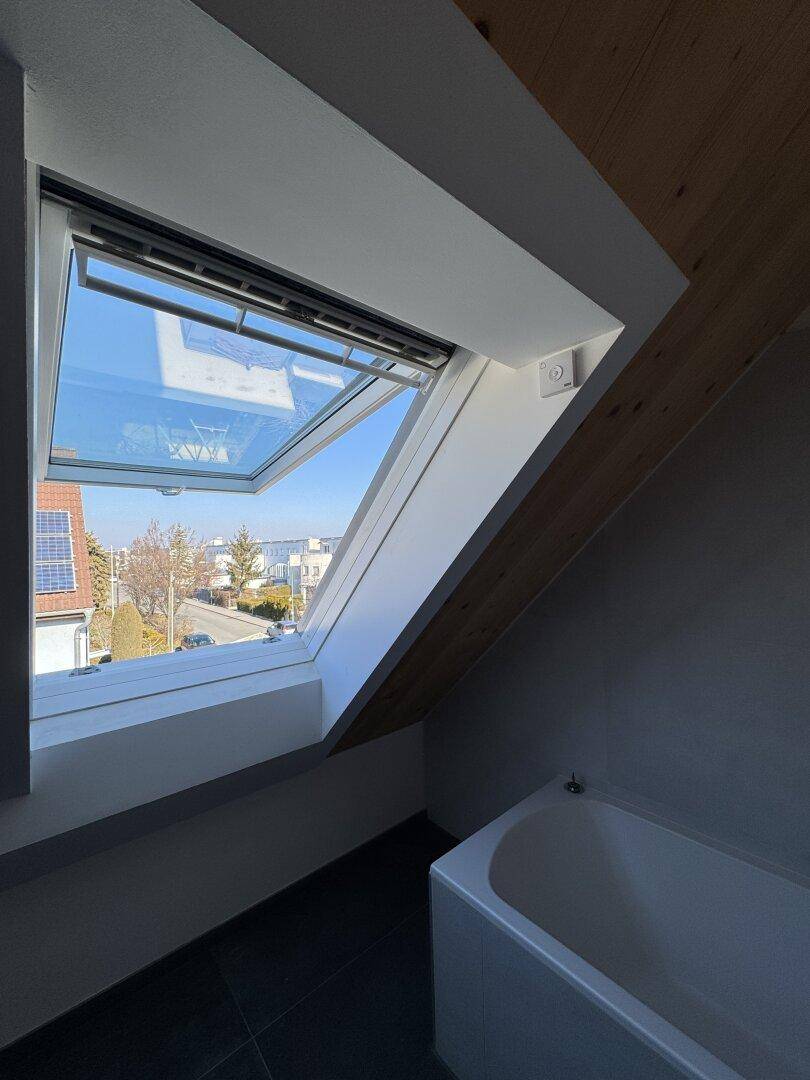 Helles Badezimmer im Dachgeschoss mit Badewanne und großem Dachfenster, das viel Tageslicht hereinlässt.