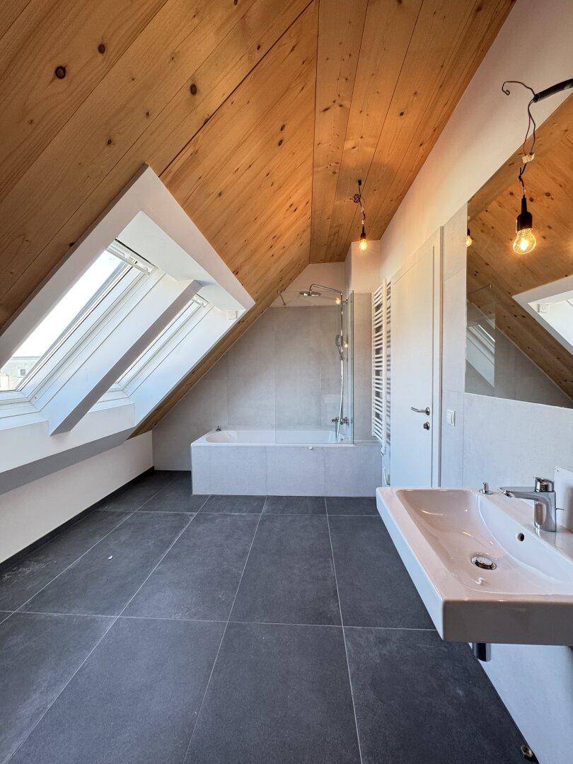 Geräumiges Badezimmer mit Badewanne, Dusche, Einzelwaschbecken und mehreren Dachfenstern.