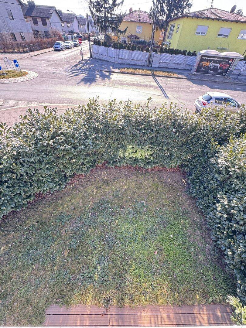 Blick von oben auf eine Straße mit Kreisverkehr und umliegende Häuser, begrenzt durch eine grüne Hecke.