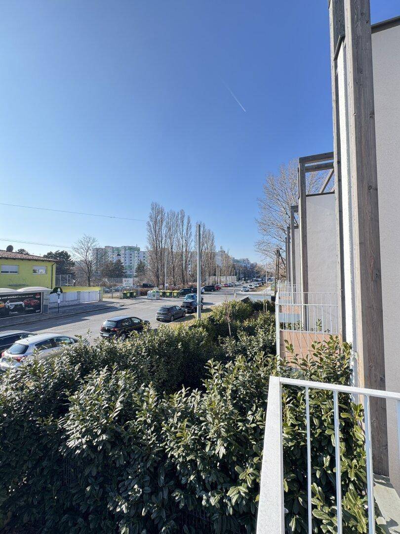 Weitblick von einem Balkon auf eine belebte Straße mit parkenden Autos und Gebäuden im Hintergrund.