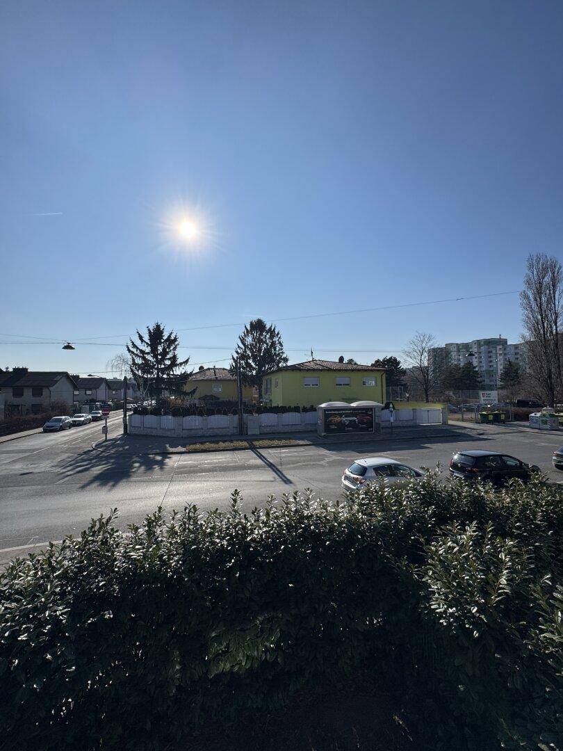 Sonniger Ausblick auf eine Kreuzung mit Kreisverkehr und umliegende Wohngebäude unter blauem Himmel.